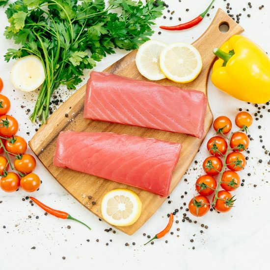 Salmon on a wooden board with vegetables around it