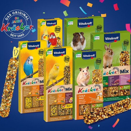 Verschiedenen Kr&auml;cker-Produkte von Vitakraft f&uuml;r V&ouml;gel und Nager auf blauem Hintergrund mit Konfetti und St&ouml;rer "60 Jahre Kr&auml;cker"